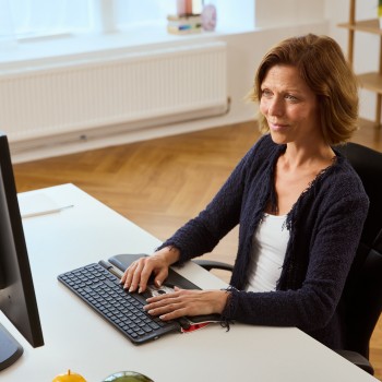 Contour Rollermouse Red Plus and Balance Mid-Size keyboard for ergonomic wor... A person working on a computer using the Contour Rollermouse Red Plus and Balance Mid-Size keyboard in a bright...