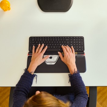 Contour Design Rollermouse Red Plus and Balance keyboard in use A person is using a black Contour Design Rollermouse Red Plus device and a medium-sized wireless keyboard on a light-colored desk.