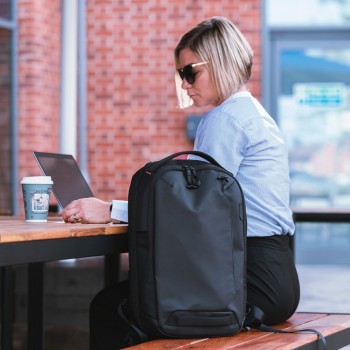 Targus Commuter EcoSmart 16" backpack for stylish work Black Targus Commuter EcoSmart backpack 16 inches on a table outdoors, a woman working on a laptop.